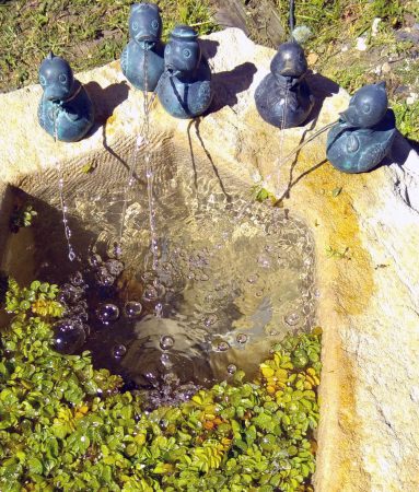 Mehrere Metall-Enten spucken Wasser in ein Steinbecken