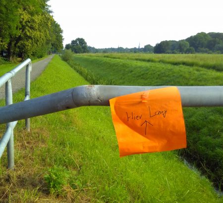 Orangefarbener handgeschriebener Zettel an einem Brückengeländer: "Hier lang".