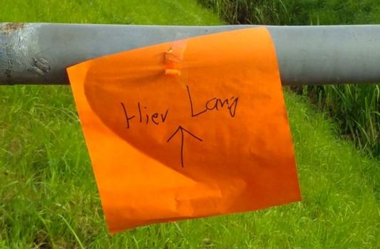 Orangefarbener handgeschriebener Zettel an einem Brückengeländer: "Hier lang".
