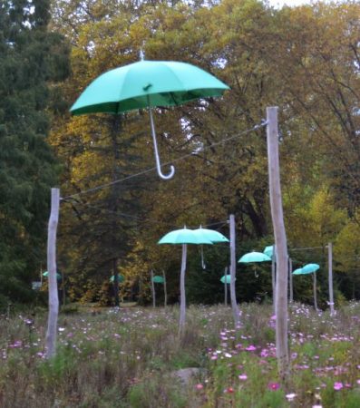Mehrere grüne Regenschirme schweben über einer Wiese.