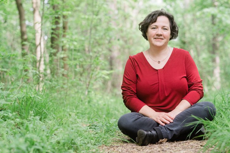 Portrait: Katja in rotem Shirt sitzt auf dem Waldboden