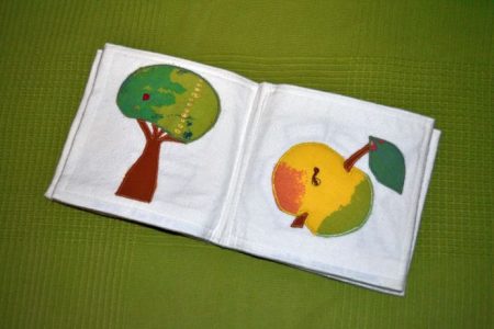 Ein Stoffbuch für Kleinkinder, die aufgeschlagenen Seiten zeigen einen Baum und einen Apfel