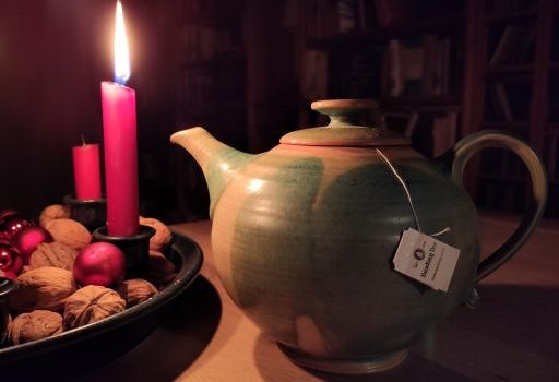 Bild zur Weihnachtsgeschichte: eine Teekanne neben einer brennenden Kerze am Adventskranz